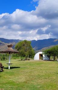 a field with a tent and a table and a umbrella at Glamping - Sol de Rumihuasi in San Luis