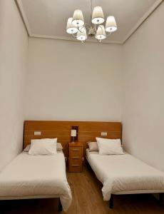 2 bedden in een kamer met witte muren en een kroonluchter bij Lersundi 3 in Bilbao
