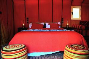 a red bed with two ottomans in a bedroom at Merzouga Paradise Luxury Camp in Merzouga