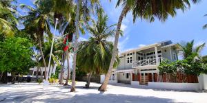 ein weißes Gebäude mit Palmen davor in der Unterkunft The Fulhadhoo Beach Cottage in Fulhadhoo