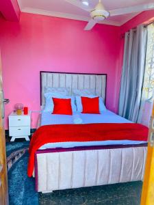 een roze slaapkamer met een groot bed met rode kussens bij The central Heartbeat Haven Intercity in Dar es Salaam