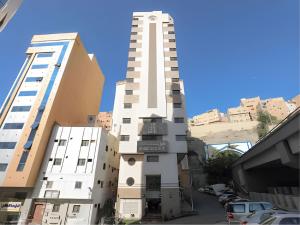 a tall white building in front of some buildings at Nasamaat Ajyad Hotel in Mecca