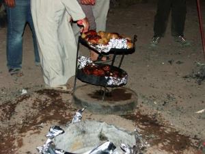 une personne prépare de la nourriture sur un grill extérieur dans l'établissement Al-Hamima Al-Abbasiya village, à Al Ḩumaymah al Jadīdah