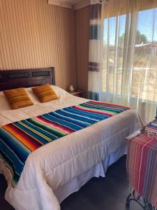 Una cama con una manta colorida y una ventana en Retiro Bajoestrellas en San Pedro de Atacama