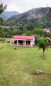 una casa bianca con un tetto rosso in un campo di C O Z Y Hut At Country Club Balakot a Bālākot