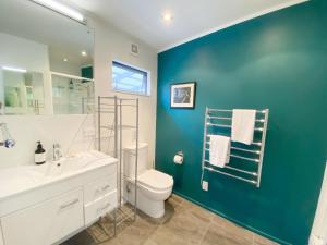 a bathroom with a white toilet and a blue wall at Delamore Cove - Kowhai - Waiheke Escapes in Matiatia Bay