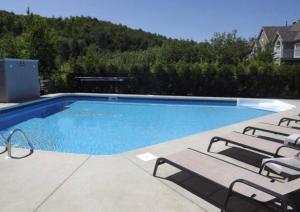 a swimming pool with lounge chairs next to it at Chalet Saint-Sauveur with heated pool during Summer and Ski in Ski out! in Saint-Sauveur-des-Monts