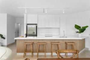 a kitchen with white cabinets and a counter with stools at Noosa Tropicana in Noosaville
