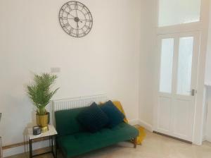 eine grüne Couch in einem Wohnzimmer mit einer Uhr an der Wand in der Unterkunft WHOLE HOUSE, Near Bury Town Centre Manchester , 3 Bedrooms, 3 En-suite House, Free Parking, Wi-Fi, Sleeps 5 in Bury