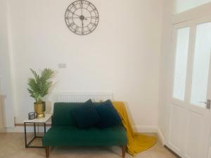 a green couch in a living room with a clock on the wall at WHOLE HOUSE, Near Bury Town Centre, 3 Bedrooms, 3 En-suite House, FREE Parking, Wi-Fi, Sleeps 5 in Bury