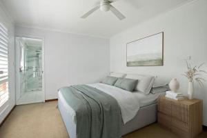 een witte slaapkamer met een bed en een plafondventilator bij Mollymook Fantastic Holiday House in Mollymook