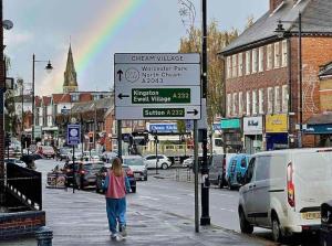 a woman walking down a street with a rainbow in the background at Flat in Cheam in Sutton