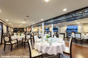 un restaurante con mesas y sillas blancas y ventanas en Amanda Legend Cruise Ha Long Bay en Ha Long