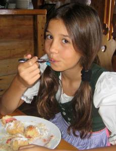 Ein junges Mädchen, das an einem Tisch mit einem Teller Essen sitzt. in der Unterkunft Landhaus Knödl-Alm in Bad Mitterndorf