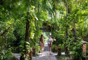 Tonys Villas & Resort Seminyak - Bali في سمينياك: سيدتان تتمشيان مع حديقة بها أشجار نخيل