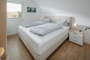 a white bedroom with a large white bed and a window at Haus an den Dünen in Norderney