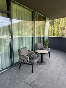 dwa krzesła i stół na balkonie z oknami w obiekcie SAVOIE Apartments Bukovel w mieście Bukowel
