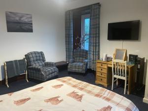 a bedroom with a bed and two chairs and a television at The Old Manse B&B in Thurso