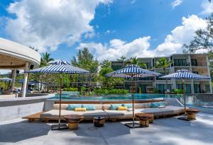 eine Terrasse mit Sofas und Sonnenschirmen neben einem Pool in der Unterkunft Le Méridien Phuket Mai Khao Beach Resort in Mai Khao Beach