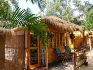 a small house with two chairs and a thatch roof at Yoga Culture Palolem in Palolem