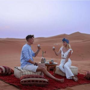 a man and woman sitting in the desert holding wine glasses at desert indigo luxury camp in Merzouga