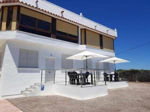 ein weißes Haus mit Stühlen und Sonnenschirmen davor in der Unterkunft Apartamentos Cap y Corp in Alcossebre