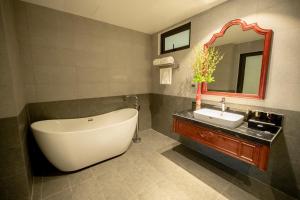 a bathroom with a tub and a sink and a mirror at Sơn Nữ Emerald Hill Hotel in Bak Kan