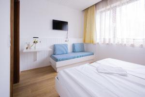 a white room with a bed and a blue chair at Pension Seerose in Pörtschach am Wörthersee