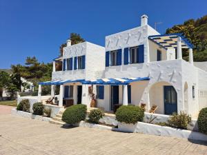 a white house with blue windows and bushes at Iremia North Kokkali Beach Leros in Gourna
