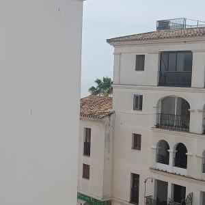 a tall white building with a palm tree behind it at Duquesa Harbour Club Aparthotel in Manilva