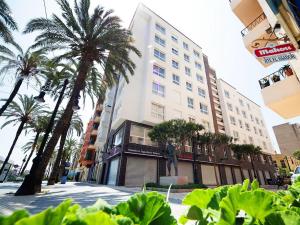 a building with palm trees and a statue in front of it at Iberflat Apartamentos Marina Suites in Grao de Castellón