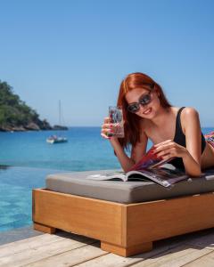 een vrouw op een bed met een boek en een drankje bij Sea Valley Lodge in Faralya