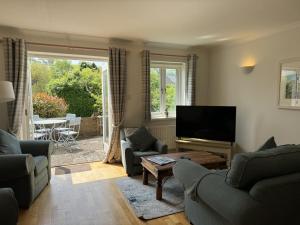 a living room with couches and a television and a table at Damson Cottage - Peaceful location, charming communal orchard & private patio garden in Dittisham