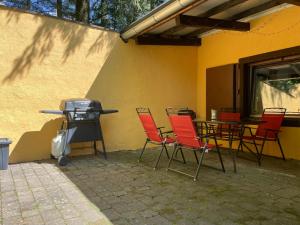 a patio with red chairs and a grill next to a yellow wall at Gemütliches Ferienhaus mit Kamin in idyllischer Waldrandlage 