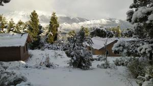una casa cubierta de nieve con montañas en el fondo en Cabañas del Gutiérrez en San Carlos de Bariloche
