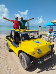 dwoje ludzi siedzących na szczycie żółtego jeepa na plaży w obiekcie Pousada Terra de Minas w mieście Natal