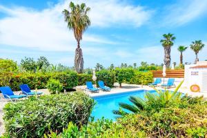 uma piscina com cadeiras azuis e palmeiras em Villa Ambrosia em Pegeia ou Pegya