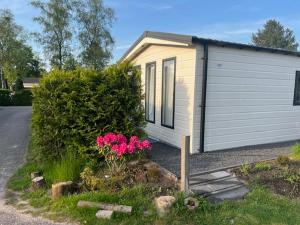 una pequeña casa con garaje y algunas flores rosas en Kerkendal en Kootwijk