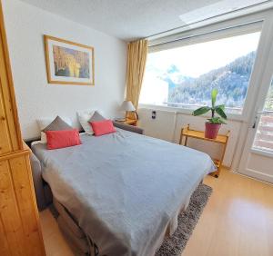 sypialnia z łóżkiem z czerwonymi poduszkami i dużym oknem w obiekcie Location Pra-Loup Vacances w mieście Pra Loup