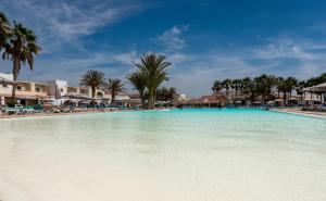 a large swimming pool with palm trees and buildings at VOI Praia de Chaves Resort in Sal Rei