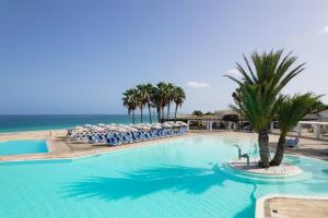 a large swimming pool with chairs and the ocean at VOI Praia de Chaves Resort in Sal Rei