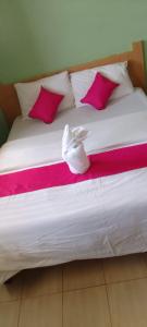 Una cama con almohadas rosas y blancas y zapatos. en Hotel Illusions, en Kakamega