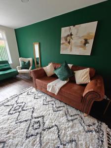 a brown couch in a living room with a green wall at 4 Bedroom Equipped House Driveway- 10 Mins to NEC JLR BHX HS2 & More- Birmingham Sutton Coldfield, Coleshill & More in Solihull +21 photos