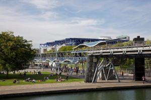 a bridge over a park with people sitting on the grass at Charming & cocooning flat - Canal de l’Ourq in Pantin
