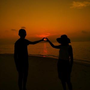 una pareja de pie en la playa viendo la puesta de sol en Gaskara Guesthouse, en Shaviyani Atoll