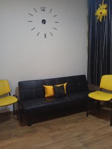 um sofá preto num quarto com cadeiras amarelas e um relógio em Апартамент в Новобудові Стрийська Автовокзал em Lviv