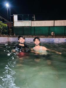 2 hommes nageant dans une piscine la nuit dans l'établissement Sun n moon farm, à Noida