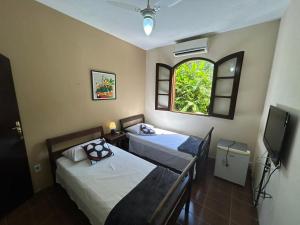 two beds in a room with a window and a television at POUSADA RECANTO DA LADEIRA in Paraty