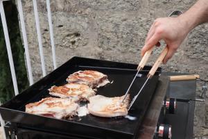 une personne qui cuisine de la nourriture sur un grill avec des baguettes dans l'établissement Maison de Village 18ème Siècle Familiale 3 Chambres, à Mus