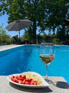 a glass of wine and a plate of fruit next to a pool at Drinska Prica - Vikendica na Drini in Loznica
